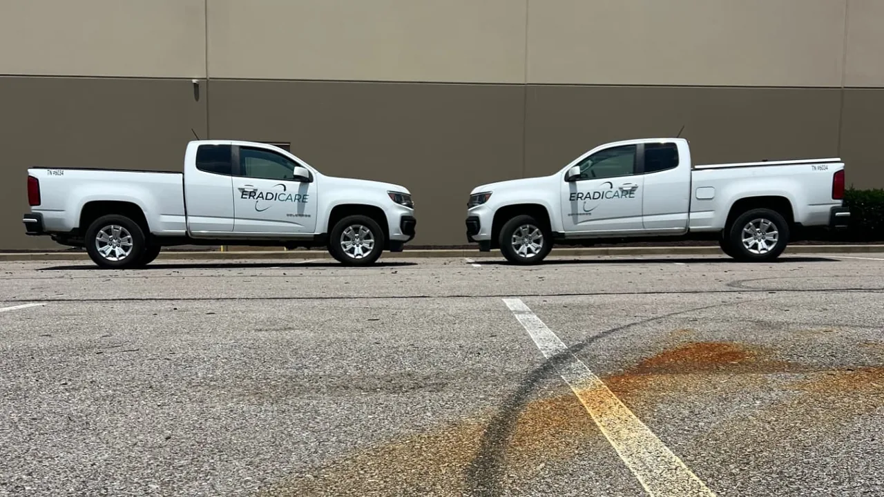 Two white Eradicare service trucks parked outside a commercial building in Tennessee
